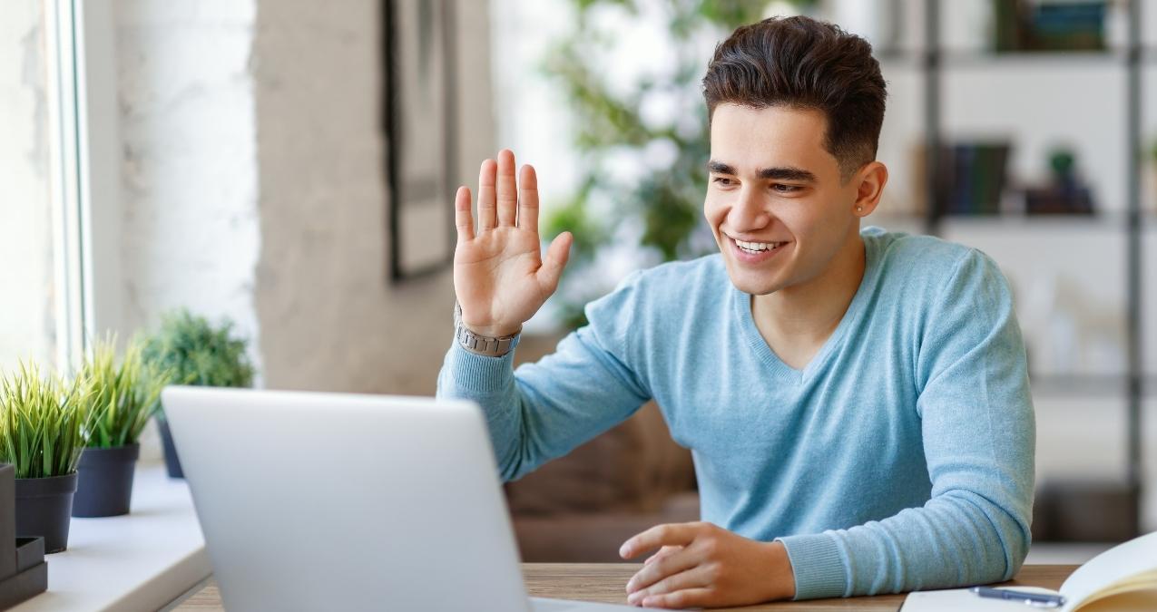 male student in blue sweater waving at laptop